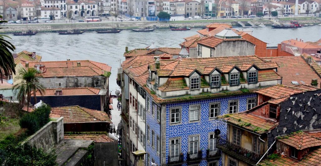 Blick von oben auf ein blaues Haus mit einem relativ ramponierten Dach aus roten Pfannen. Dahinter fließt der Douro.
