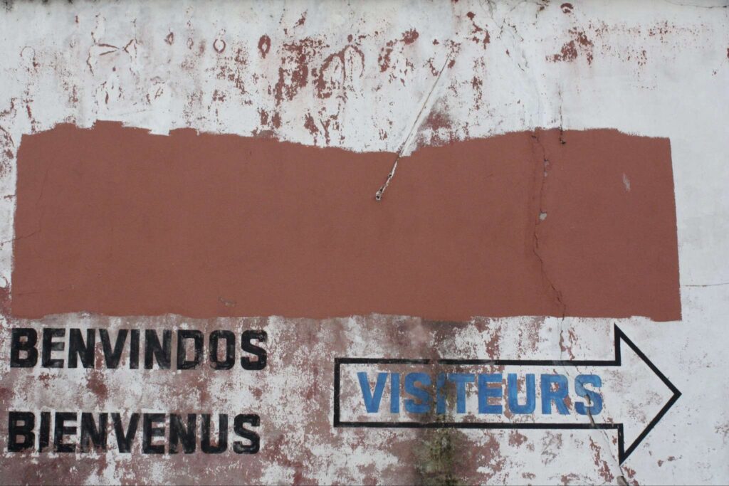 Verwitterte Wandmalerei mit den Worten Benvindos / Bienvenus  Visiteurs. 